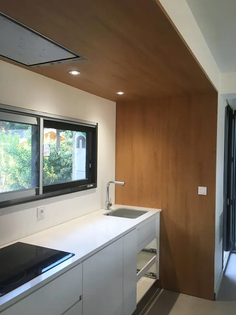 Cuisine sur mesure blanche sous rampant, plan de travail clair et habillage de plafond en bois