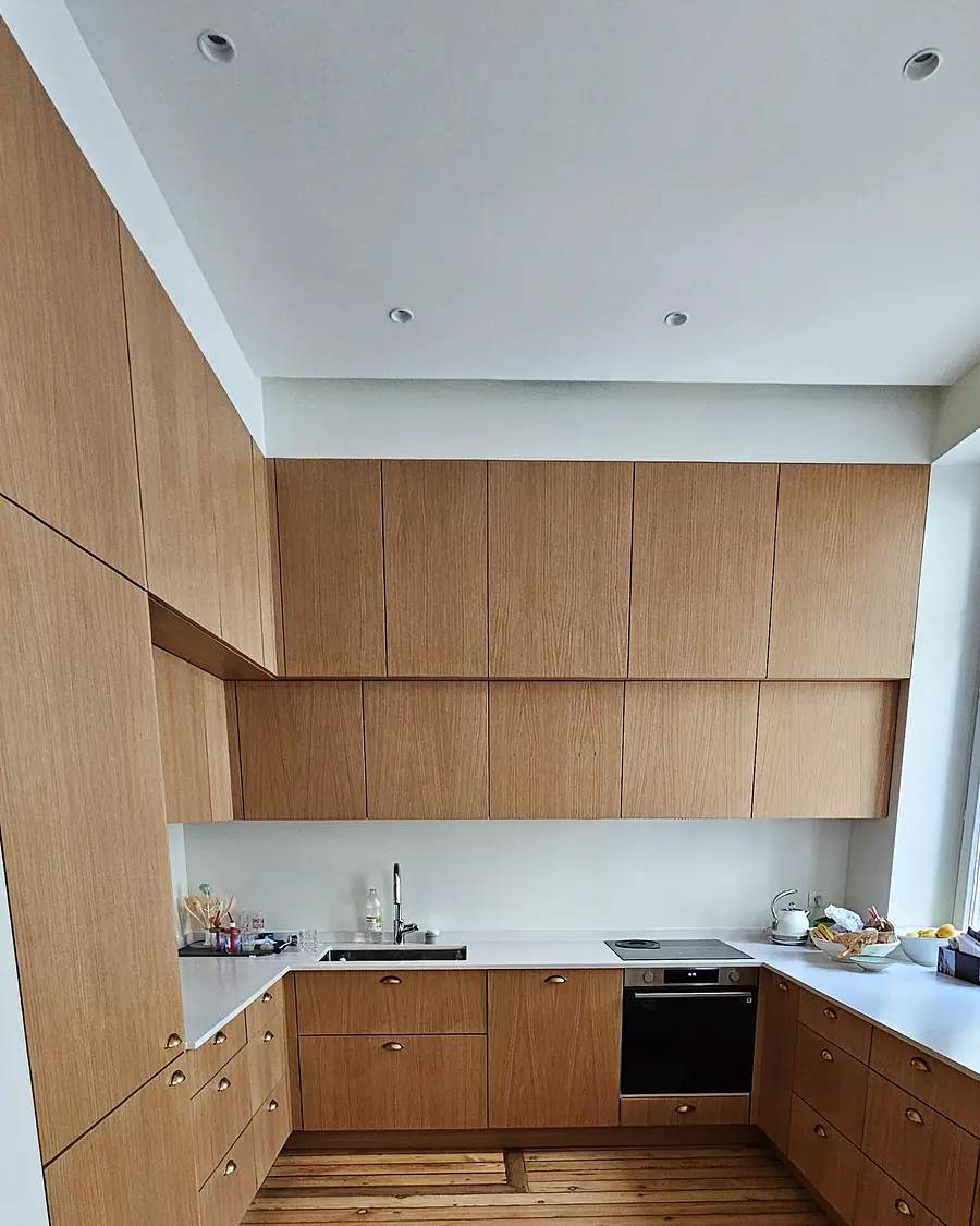 Cuisine en U sur mesure en chêne clair avec plan de travail blanc, meubles hauts jusqu'au plafond et poignées laiton