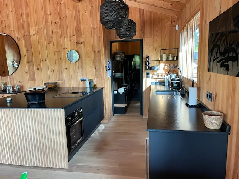 Cuisine bois sur mesure avec îlot cannelé, plan de travail noir mat, cave à vin intégrée et rangements toute hauteur