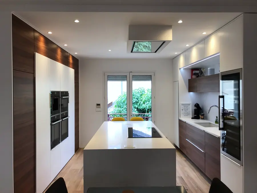 Longue cuisine sur mesure avec îlot central, plan de travail en quartz et colonnes en placage bois