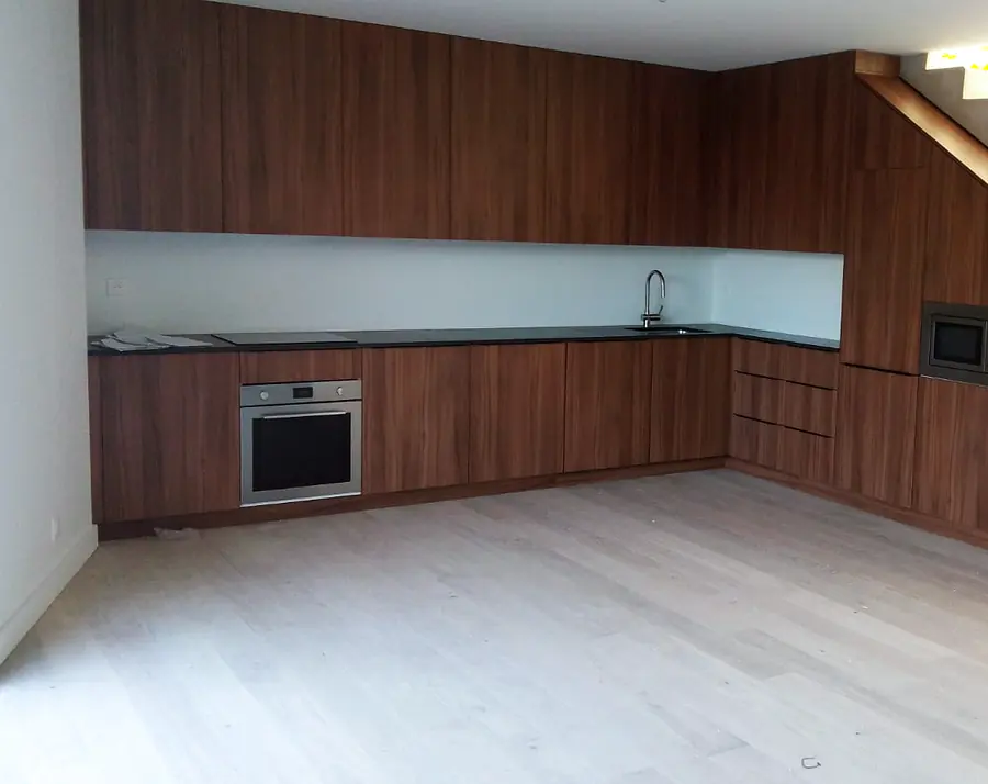 Cuisine sur mesure en noyer épousant un escalier, plan de travail continu et crédence en verre